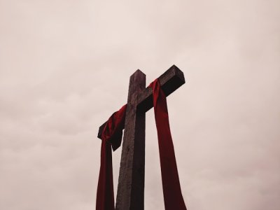 Image shows a low angle view of a cross with a red garment draped over the cross piece.